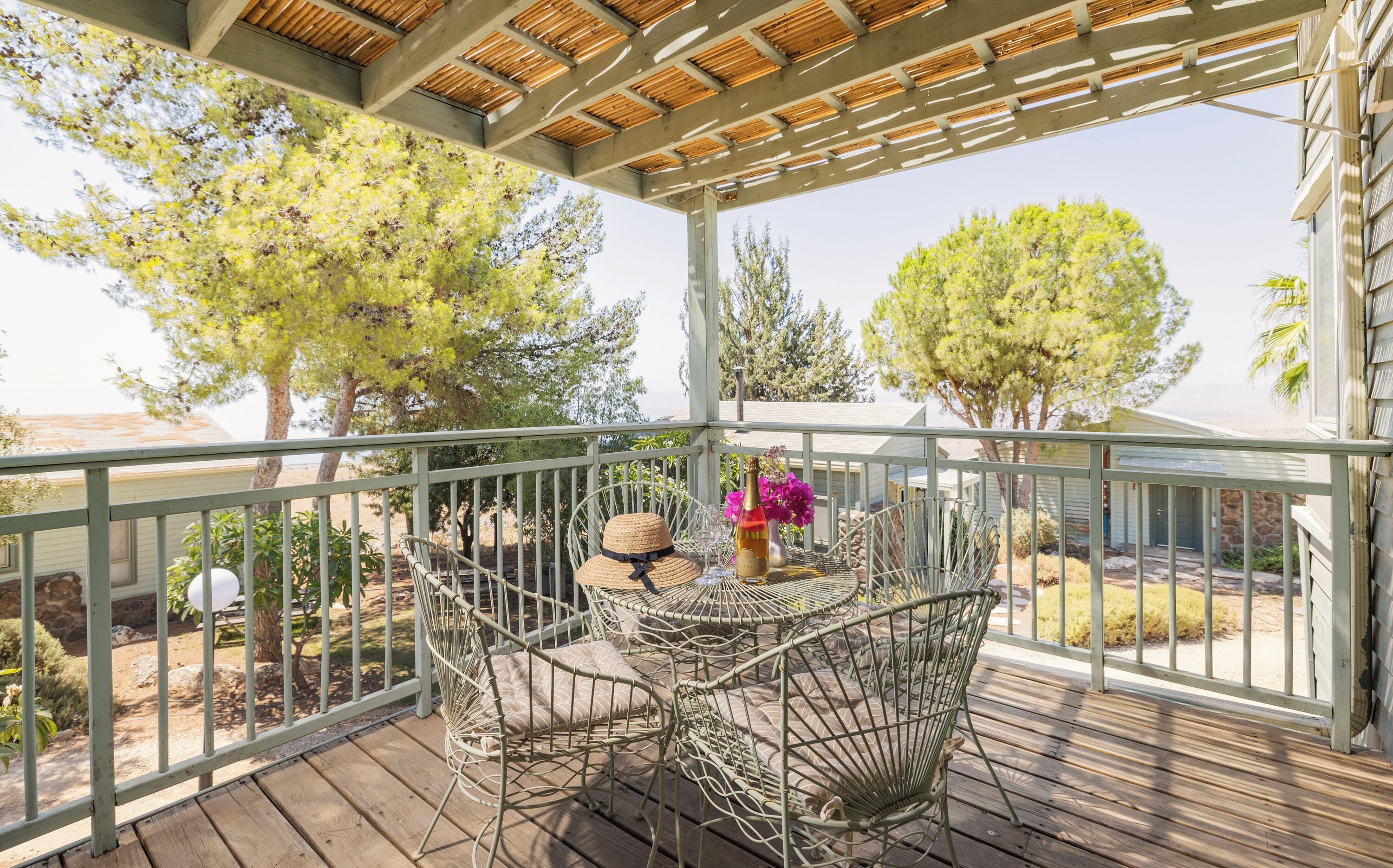 A covered outdoor area with wicker chairs and a table, surrounded by trees and a view of the beach.