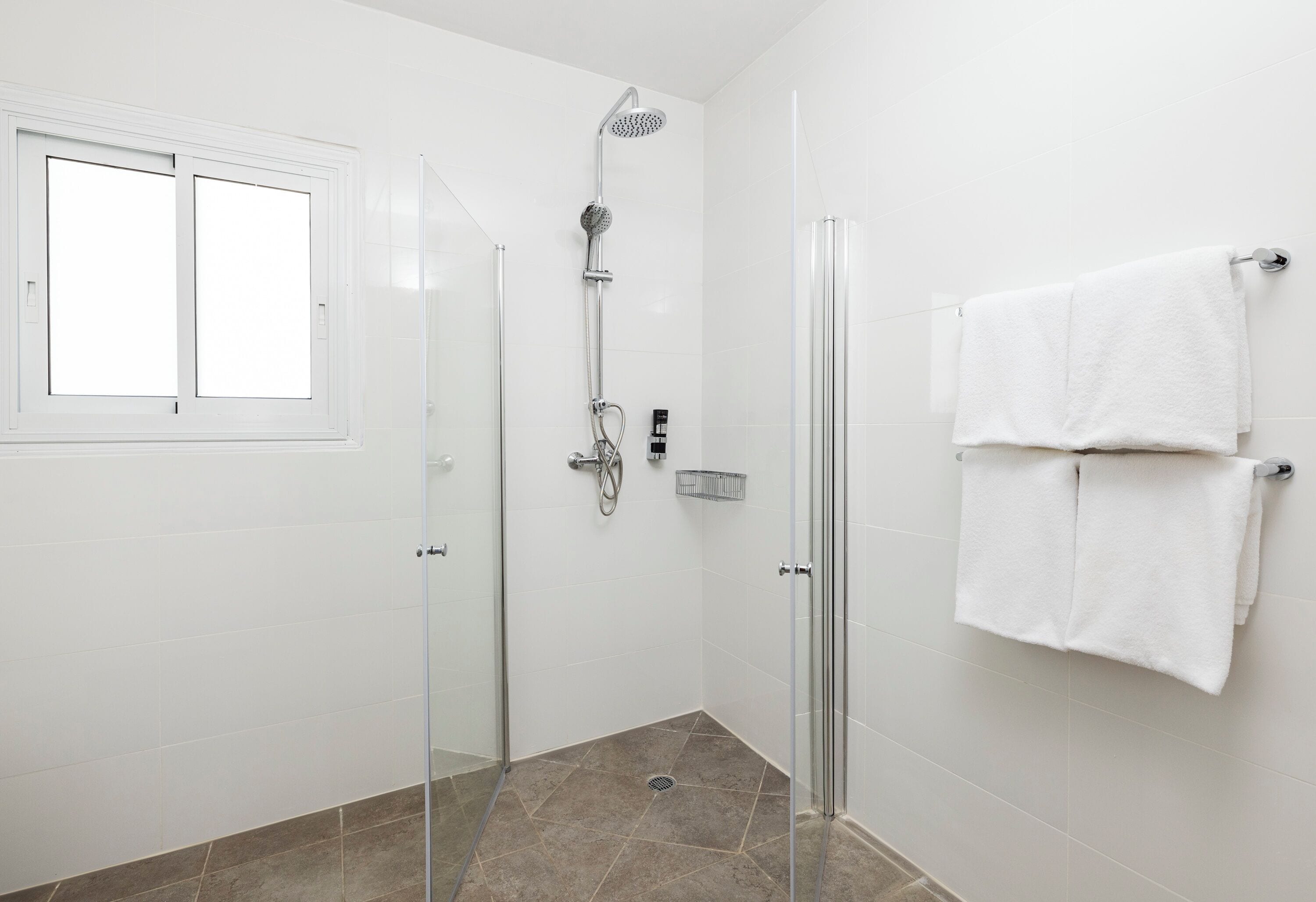 Une salle de bain moderne avec une douche à parois de verre, un porte-serviettes blanc et une fenêtre équipée de stores.