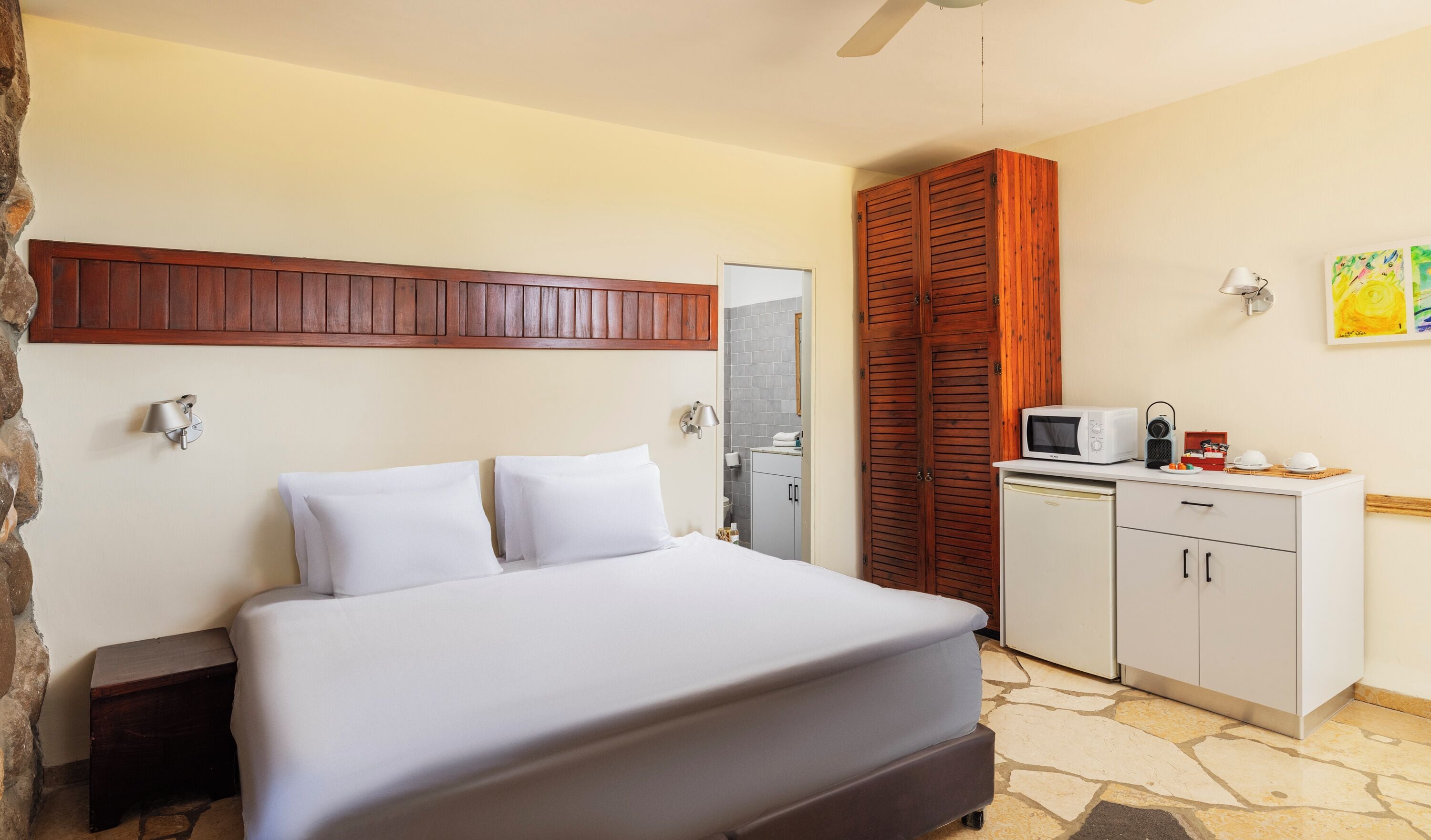 Una habitación de hotel con una cama, una kitchenette pequeña, un armario de madera y piso con estampado de piedra.