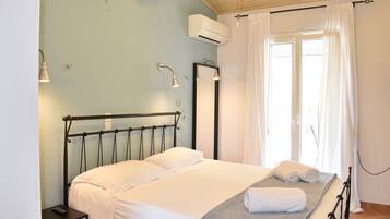 A neatly made bed with white linens, a bedside table with a remote control, and a window with white curtains.