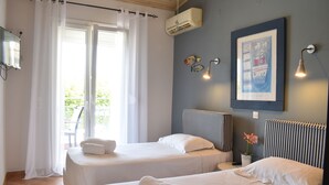 A hotel room with two beds, a large window with curtains, a wall-mounted air conditioner, a framed picture, and a small potted plant. - Simatos Apartments and Studios (Kefalonia)