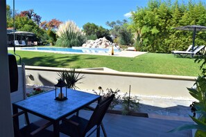 Un patio con mesa y sillas, una piscina y vistas a un jardín ajardinado.