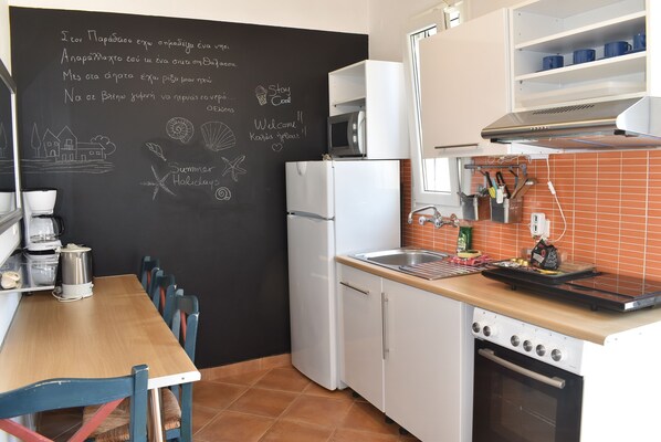 A kitchen with a chalkboard wall, white cabinets, a wooden table, and a tiled backsplash. - Simatos Apartments and Studios (Kefalonia)