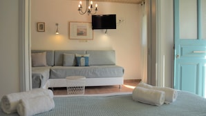A bedroom with a bed, a bedside table, a TV mounted on the wall, and a door. - Simatos Apartments and Studios (Kefalonia)