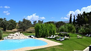 A swimming pool with lounge chairs and a grassy area, surrounded by trees and a clear sky. - Simatos Apartments and Studios (Kefalonia)