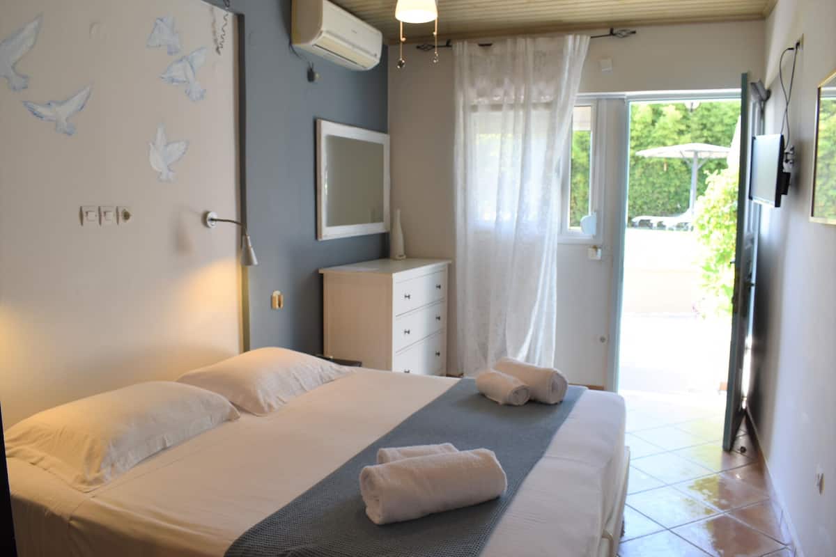 A bedroom with a bed, a bedside table, a mirror, and a window with curtains.