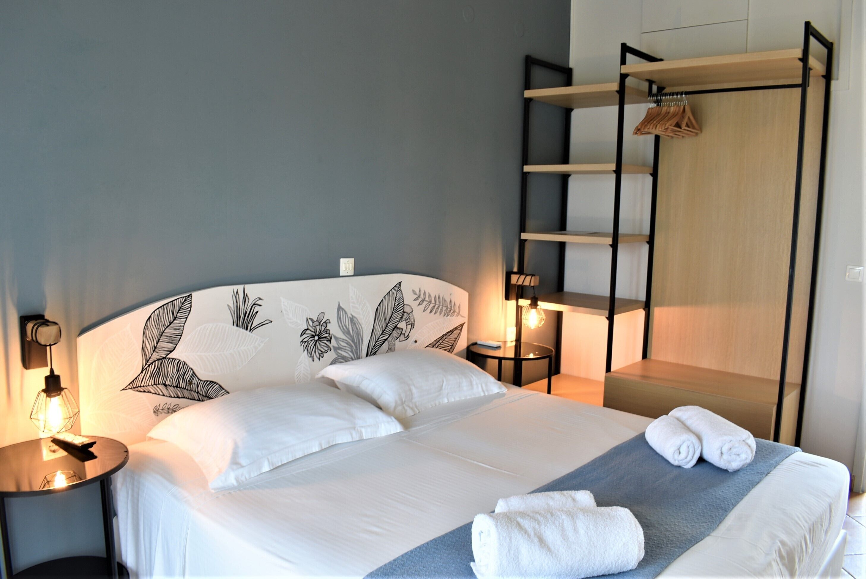 A neatly made bed with white linens, a bedside lamp, and a wall with a leaf pattern.