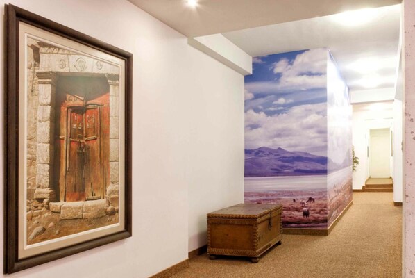 A hallway with a framed painting of a rustic door, a large mural of a landscape, and a small wooden chest.
