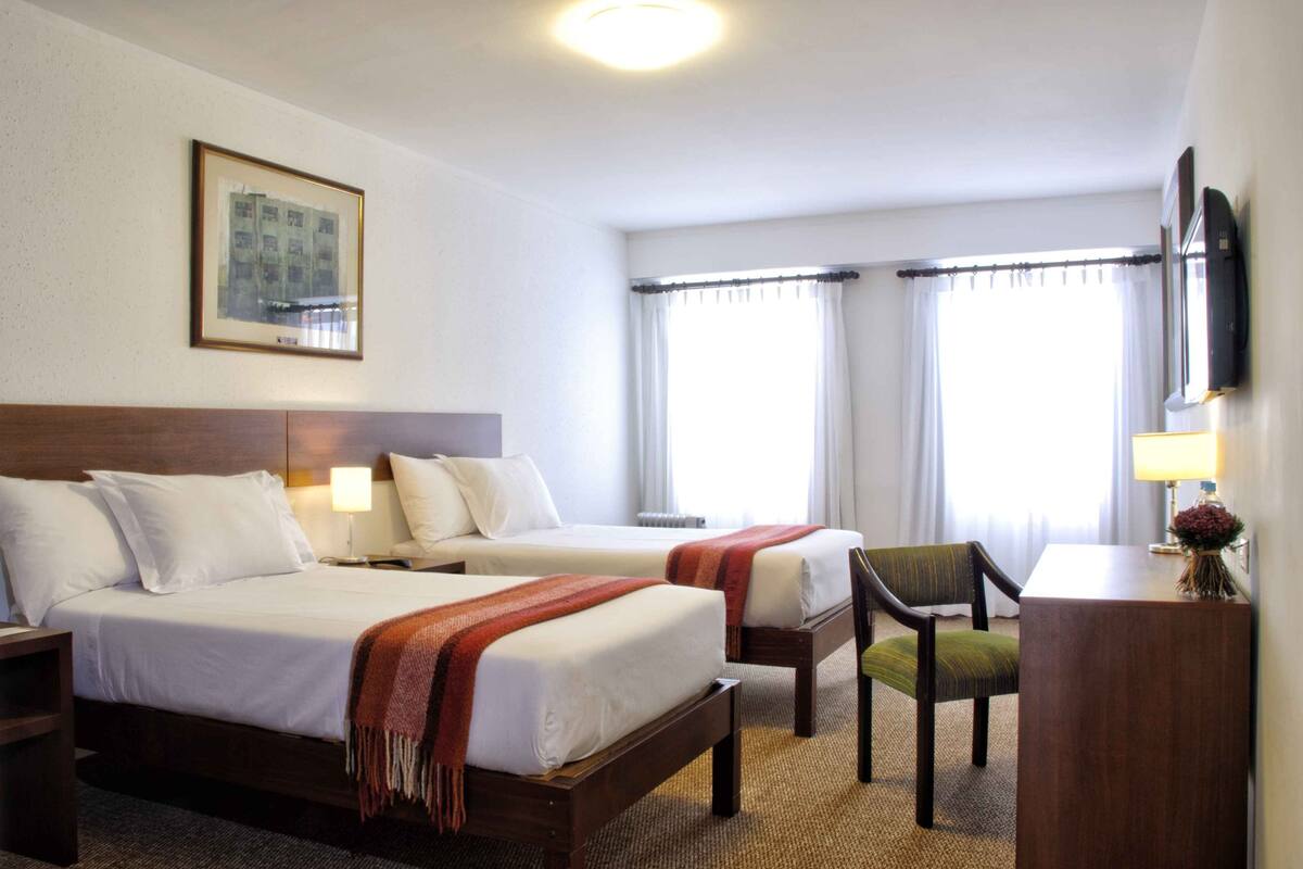 Habitación de hotel con dos camas, un escritorio, una silla, un televisor y una ventana con cortinas.
