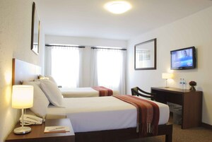 A hotel room with two beds, a desk, a chair, a TV, and a window with curtains.