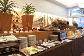 Una barra de buffet con diversos alimentos, platos y una máquina de café.