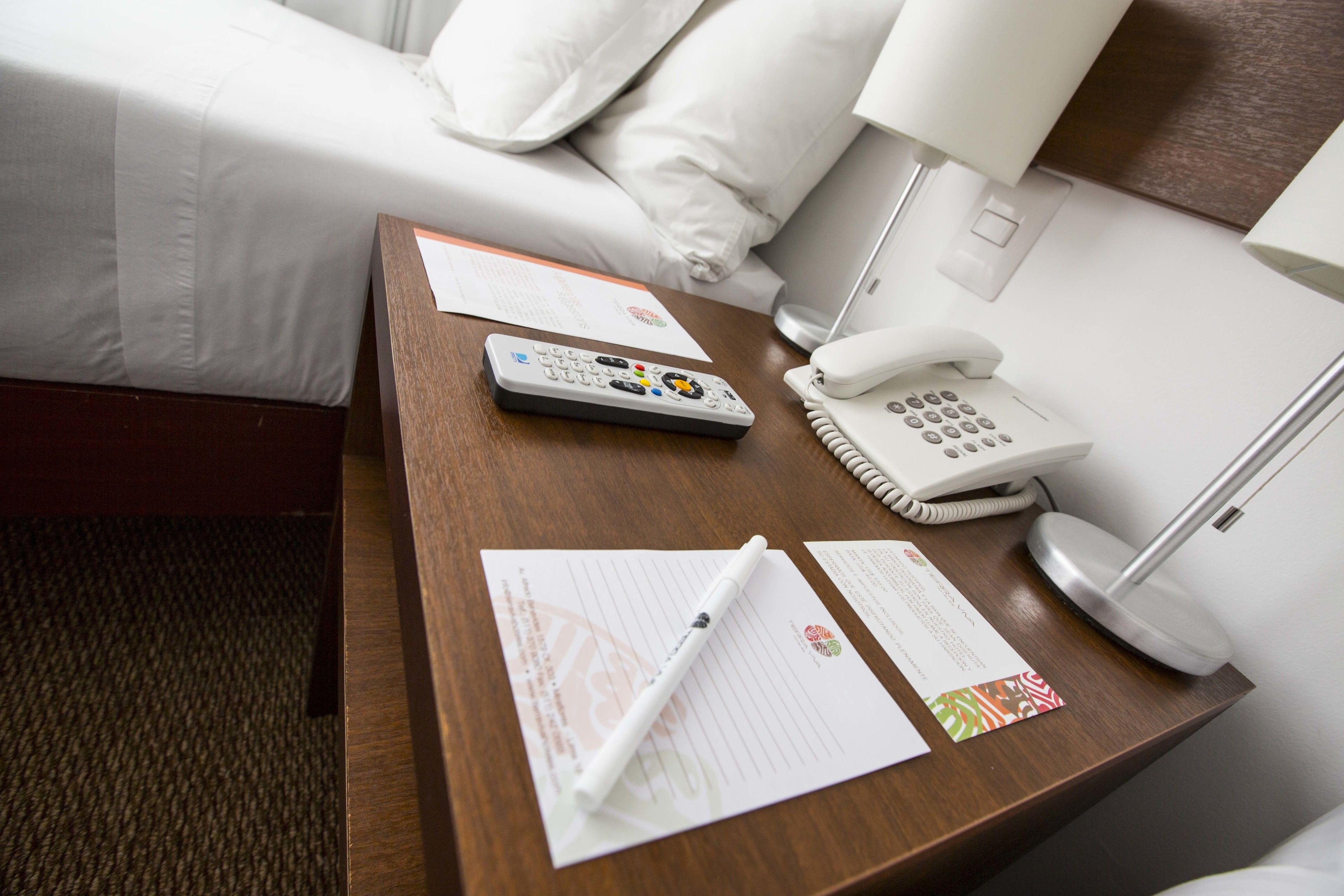 A hotel room with a wooden desk, a telephone, a remote control, and some papers.