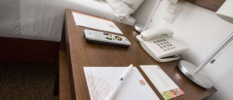 A hotel room with a wooden desk, a telephone, a remote control, and some papers.