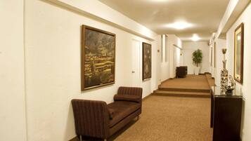 A hallway with a brown sofa, framed artwork on the walls, and a staircase leading to another level.