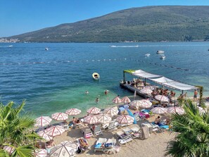 A beach with clear blue water, a boat dock, and umbrellas. - Garni Hotel Milica (Denovici)