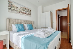 Ein Schlafzimmer mit Bett, Kissen, einem Stapel Handtüchern, einem Nachttisch, einem Gemälde und einem Kleiderschrank.