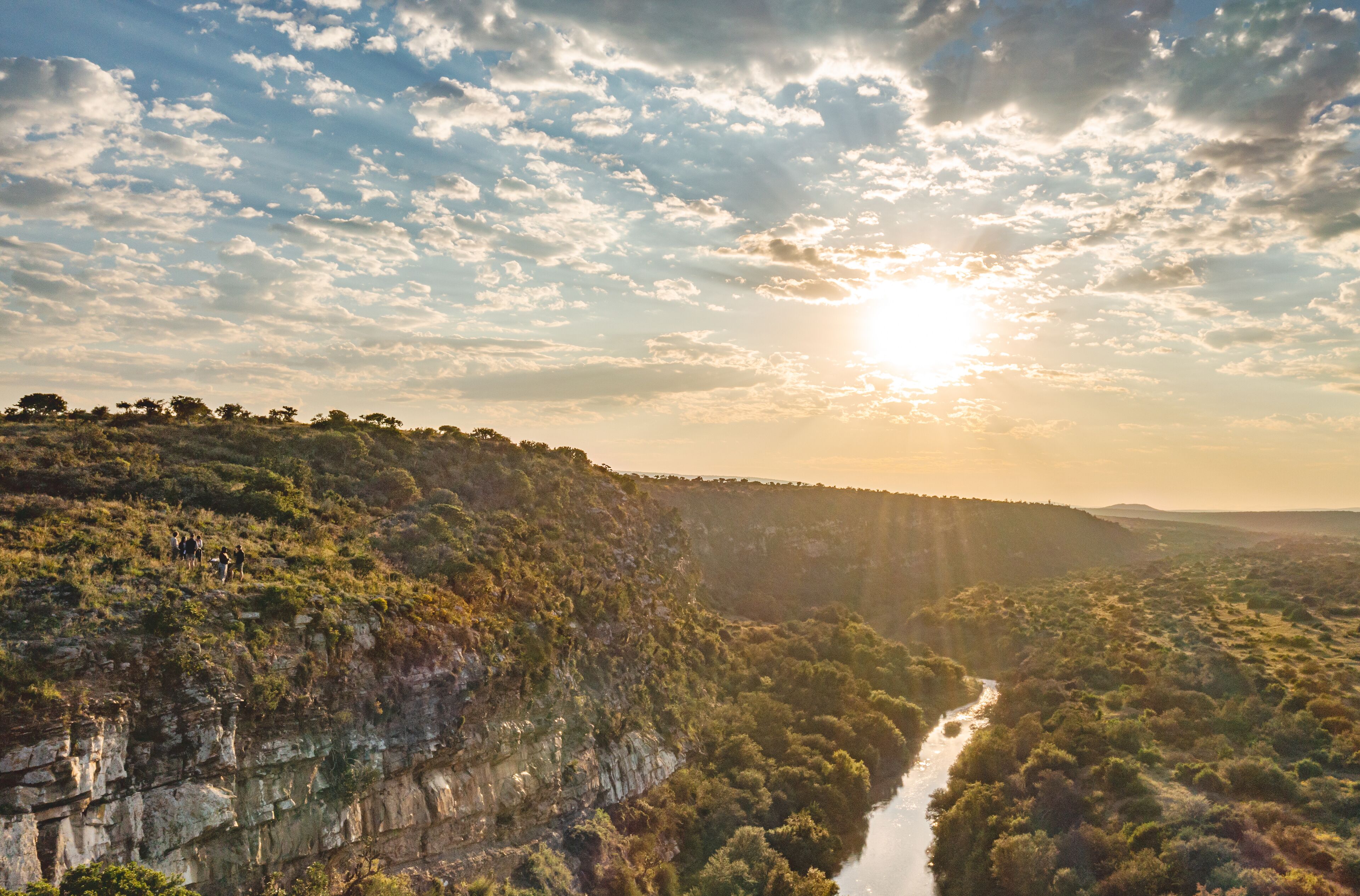 Ein Fluss, der durch eine gebirgige Landschaft fließt, mit einer Klippe auf einer Seite und einer bewaldeten Gegend auf der anderen.