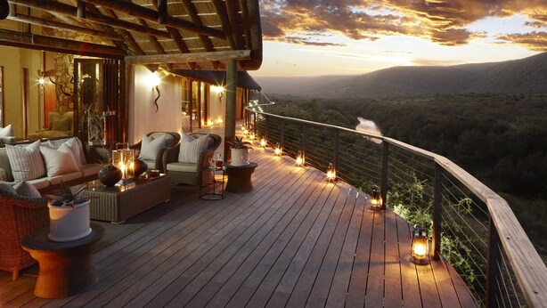 A wooden deck with outdoor seating and string lights, overlooking a mountainous landscape. - Kwandwe Great Fish River Lodge (Makhanda)