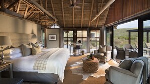 A spacious bedroom with a large bed, a desk, and seating area with a view of the outdoors. - Kwandwe Great Fish River Lodge (Makhanda)