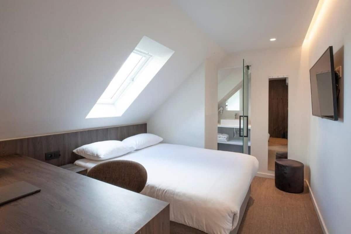 A modern hotel room with a skylight, a bed, a desk, and a mirror.
