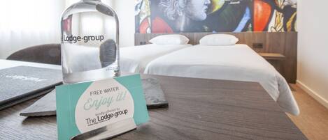 Habitación de hotel con cama, una botella de licor y un cartel que ofrece agua gratuita.