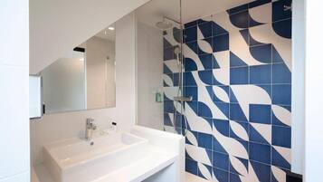 A modern bathroom with a white sink, a glass shower enclosure, and a blue and white patterned wall.
