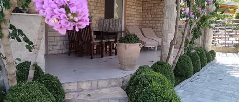 A covered patio area with a brick wall, a table with chairs, and a potted plant.