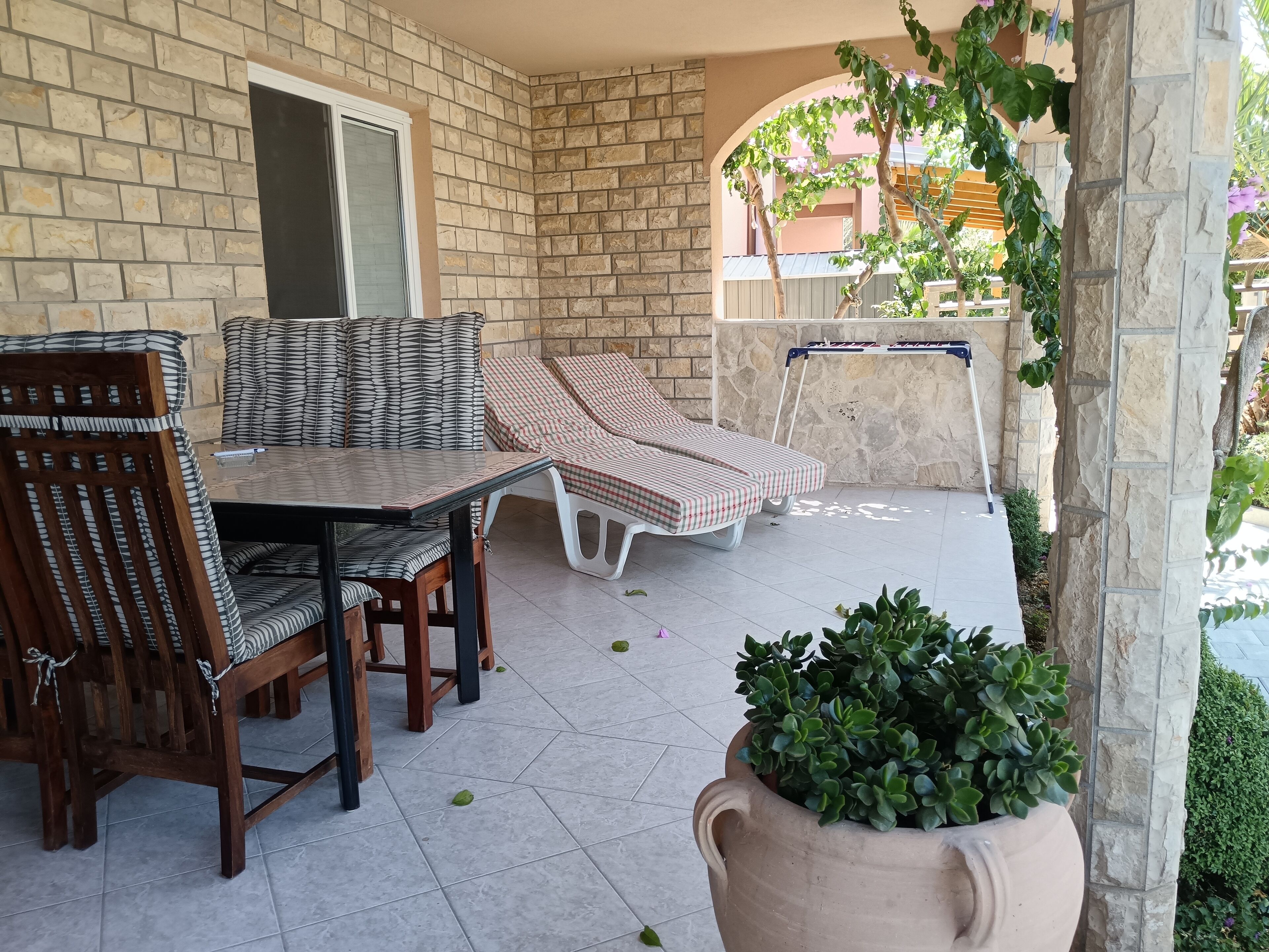 Uma área de pátio com uma mesa e cadeiras, um banco acolchoado e um vaso com planta.