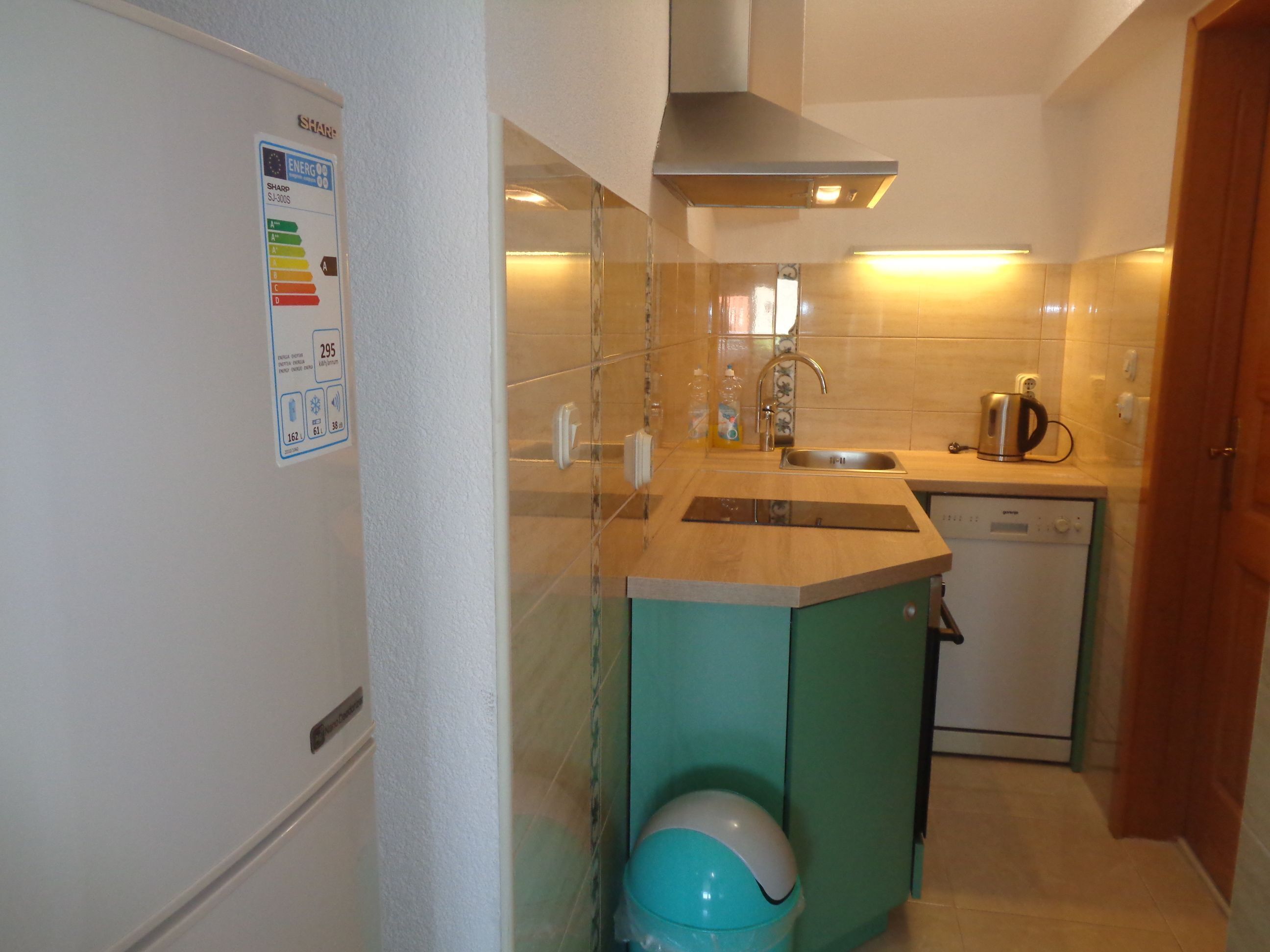 Eine kleine Küche mit Spülmaschine, Spüle und Herd. Es gibt einen Schrank mit einer türkisblauen Tür und einen weißen Kühlschrank.