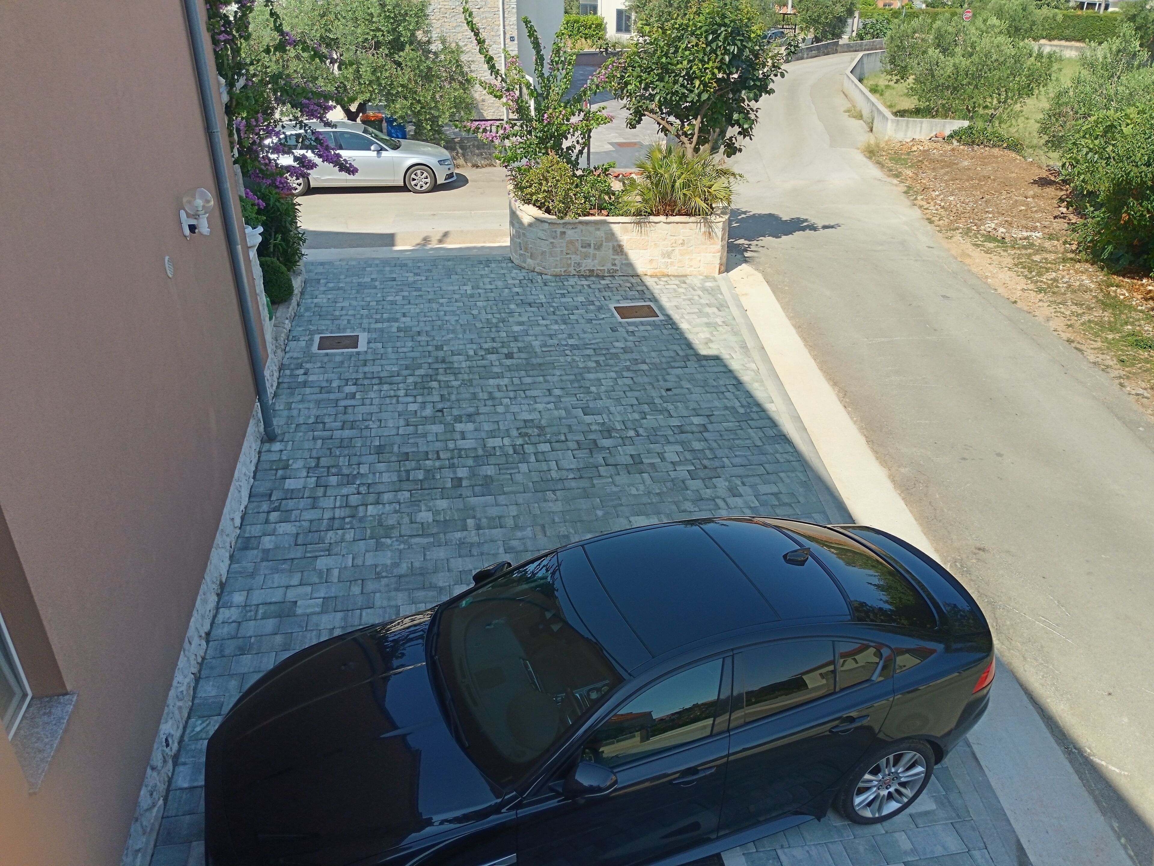 A black car parked on a paved driveway leading to a building.