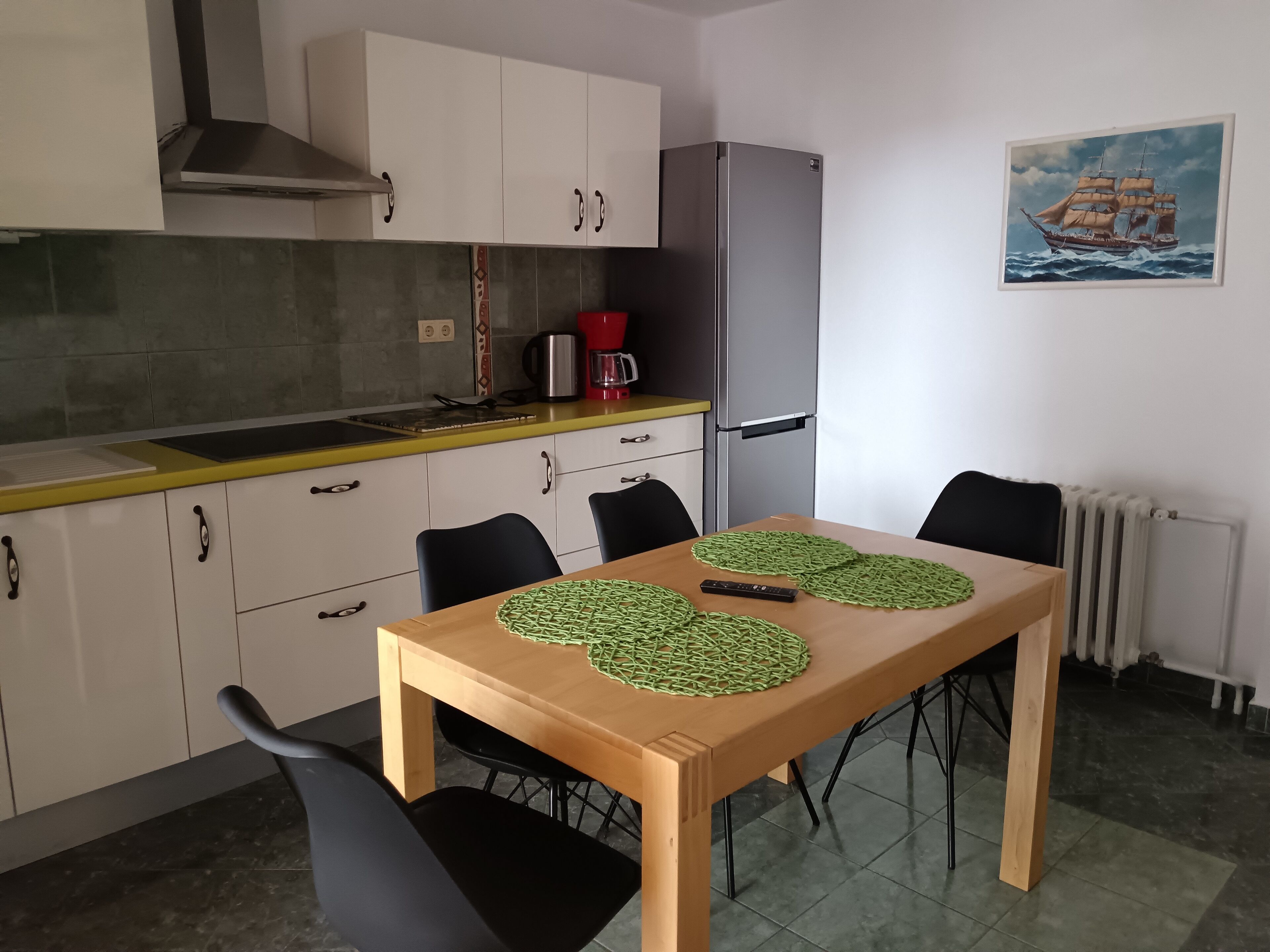A compact kitchen with a dining table, chairs, a refrigerator, and a painting on the wall.