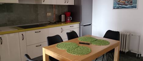 A compact kitchen with a dining table, chairs, a refrigerator, and a painting on the wall.