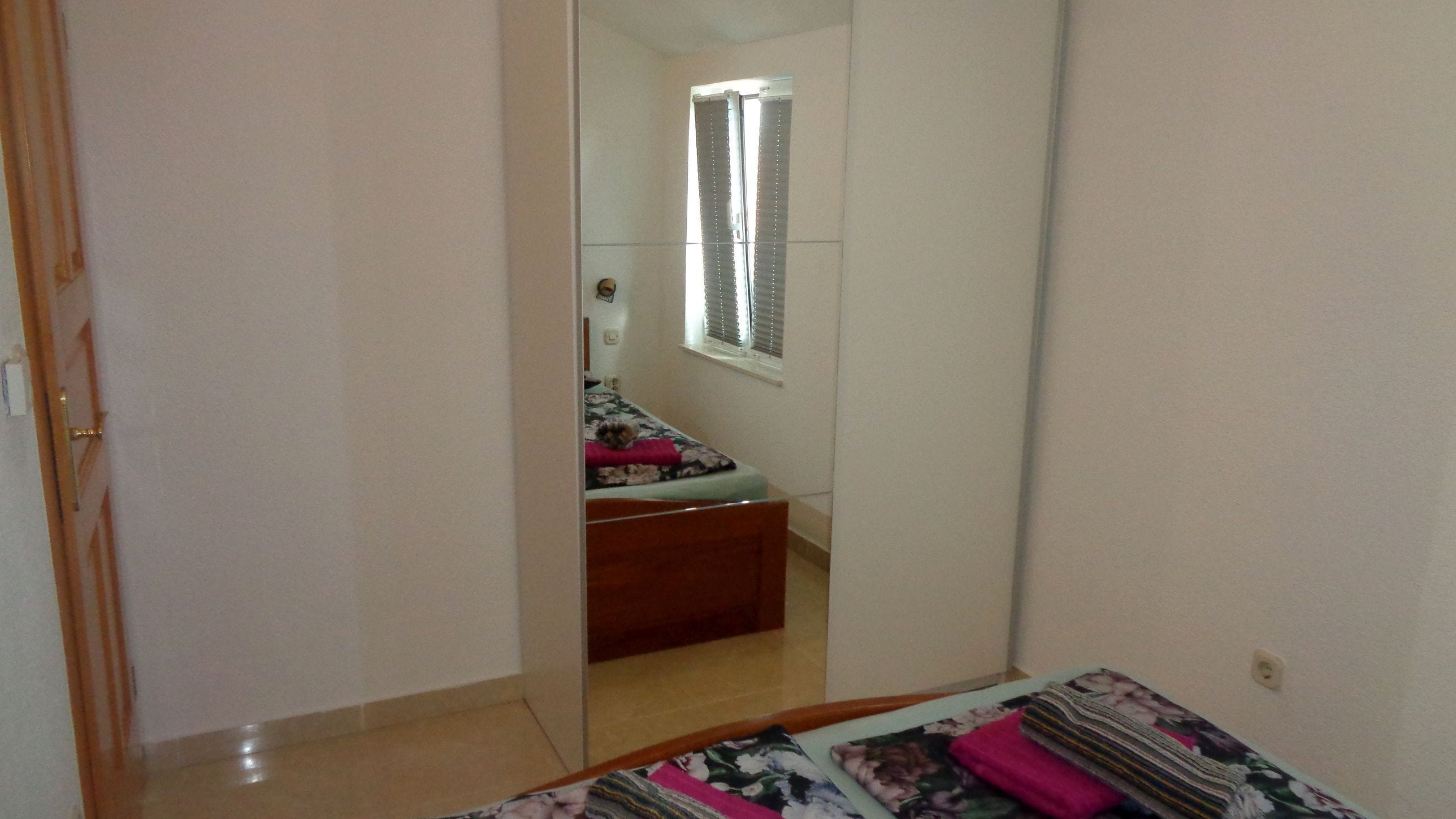 A bedroom with a bed, a mirror, and a window.