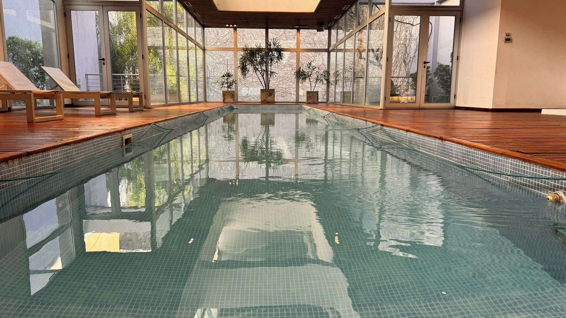 A large indoor swimming pool with clear water, wooden deck, and potted plants.