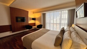A hotel room with a large bed, a TV mounted on the wall, a desk with two chairs, and a window with curtains. - Design Suites Buenos Aires (Buenos Aires)