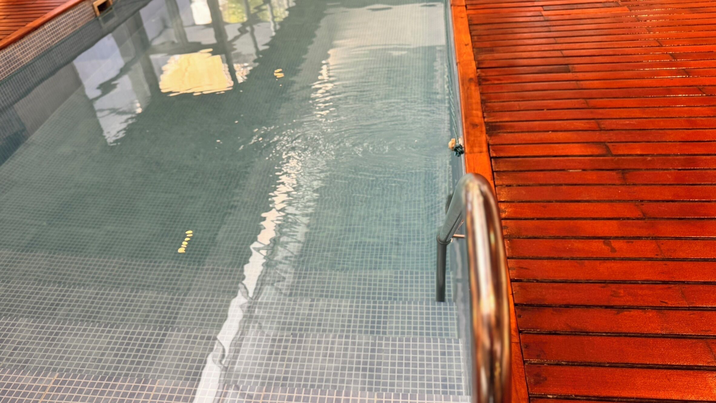 A swimming pool with a tiled floor and a wooden deck area.