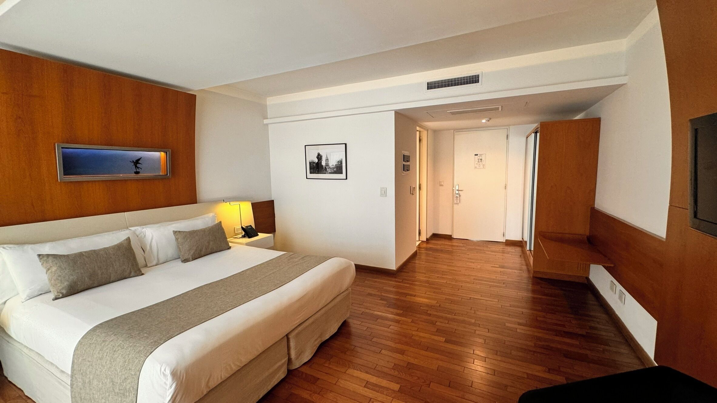Une chambre d’hôtel avec un grand lit, des boiseries, une table de chevet avec une lampe et un tableau encadré au mur.