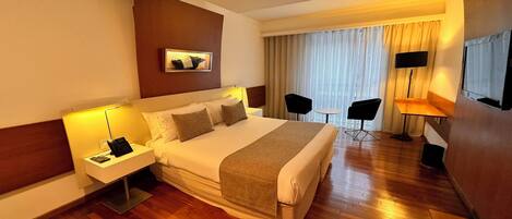 Una habitación de hotel con una cama grande, mesitas de noche con lámparas, un escritorio con una silla y un televisor en la pared.