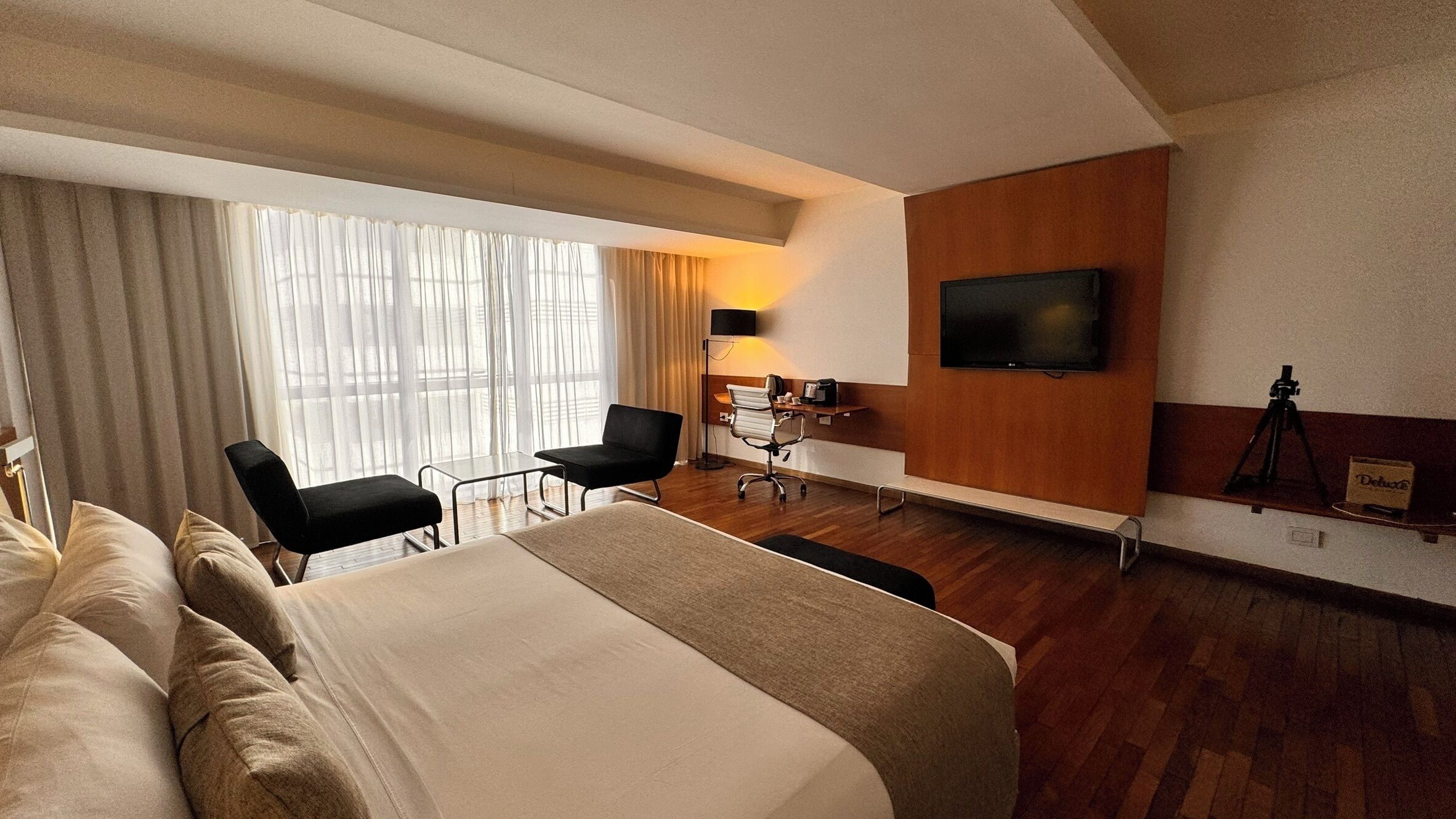 A hotel room with a bed, two chairs, a desk, a TV, and a lamp.