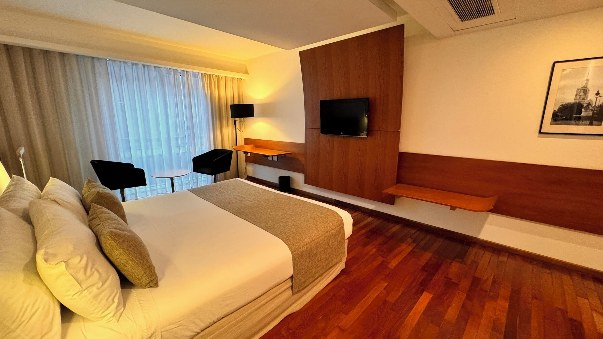 Habitación de hotel con una cama grande, un escritorio, una silla, un televisor y un banco de madera.