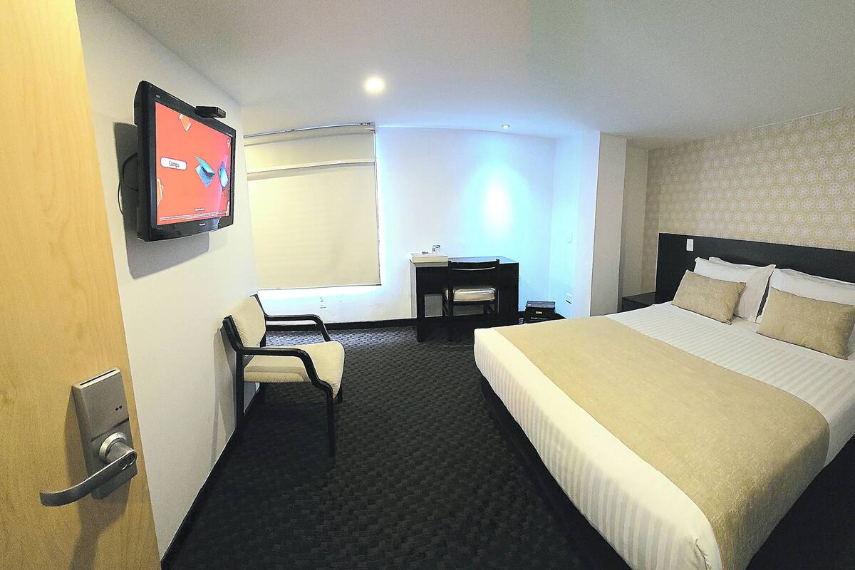 Une chambre d’hôtel avec un lit, un bureau, une chaise, une télévision et une fenêtre.
