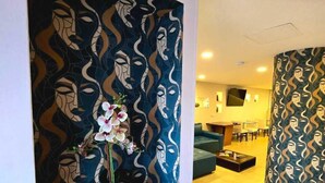 Un intérieur moderne agrémenté d’une décoration murale à motifs, d’un vase rempli de fleurs et d’un coin salon avec un canapé et une table basse.