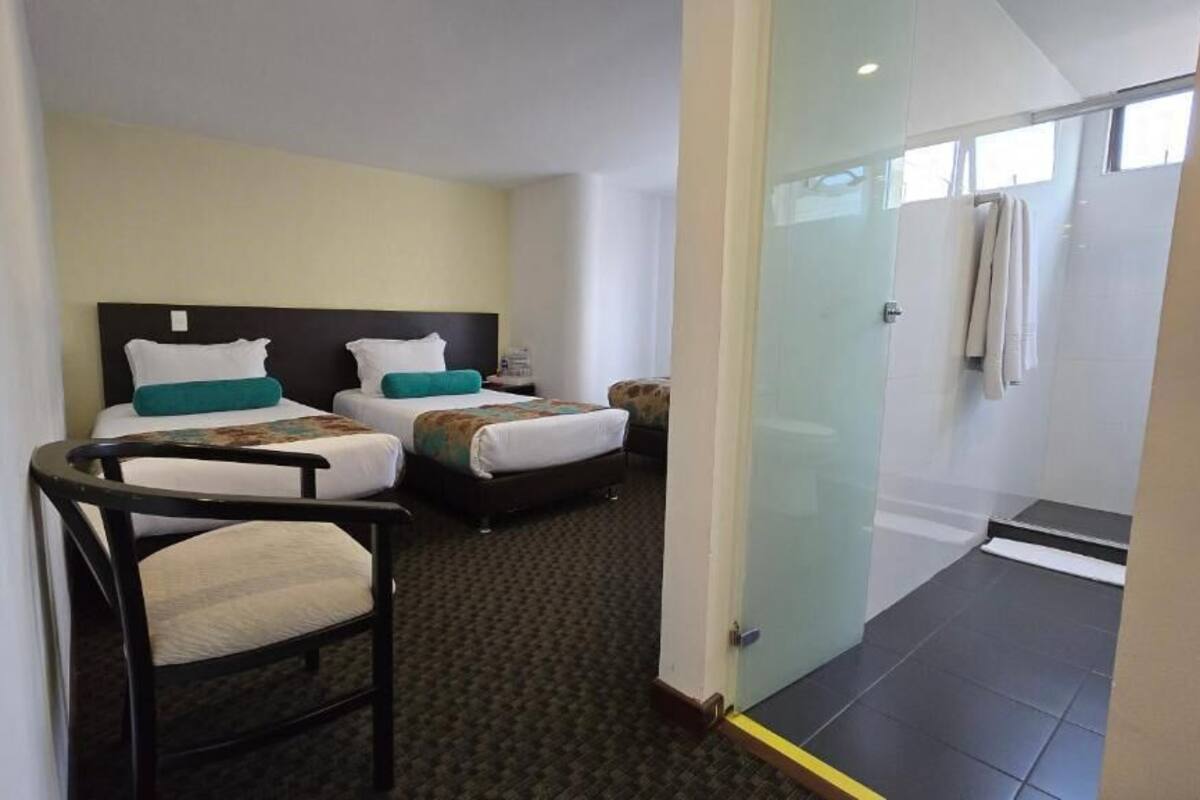 Une chambre d’hôtel avec deux lits, une chaise, une petite table et une cabine de douche en verre.
