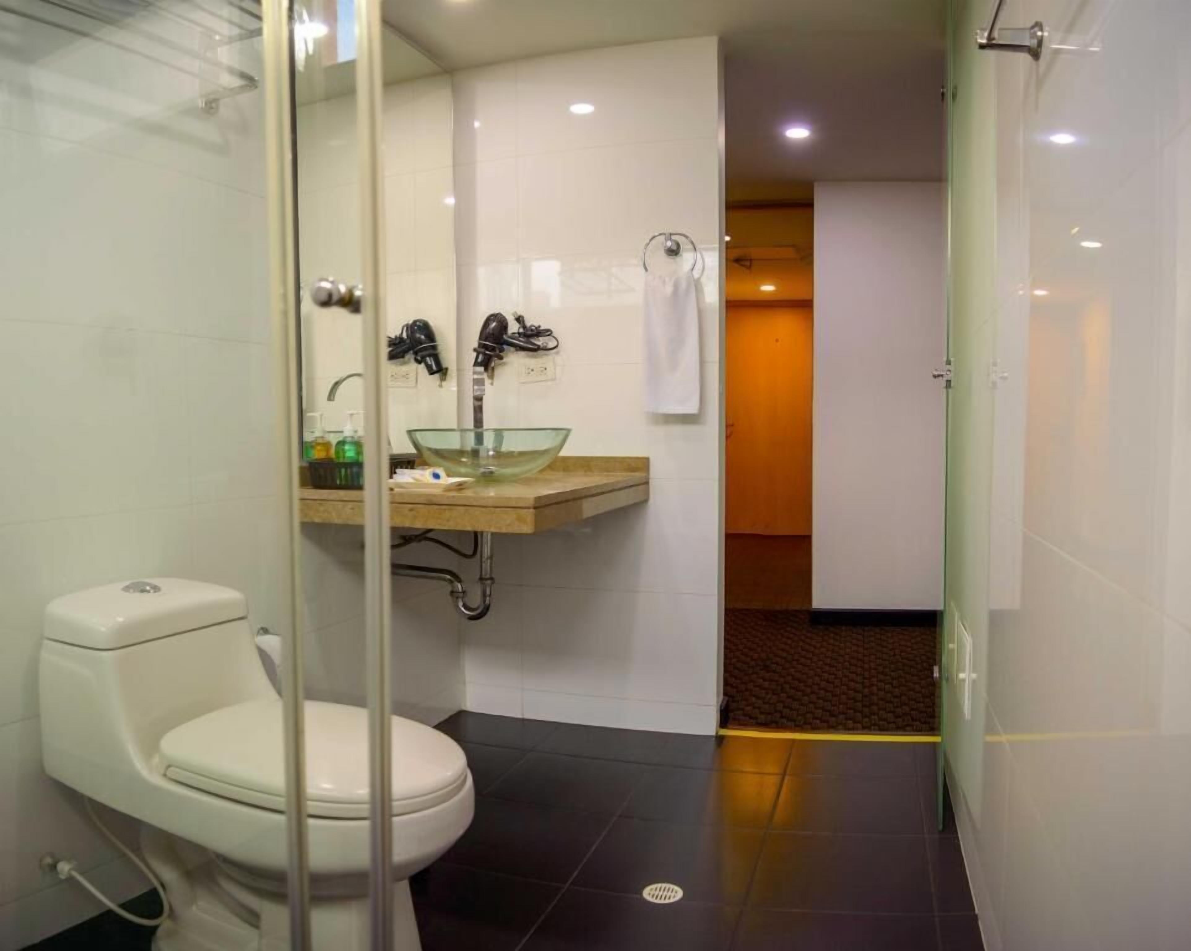 A modern bathroom with a glass shower enclosure, a white toilet, a beige sink with a glass basin, and a towel rack.