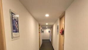 Un couloir d’hôtel avec une moquette sombre, des murs blancs et des portes de chaque côté.