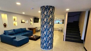 Un hall d’hôtel moderne avec un canapé bleu, une colonne à motifs et un escalier.