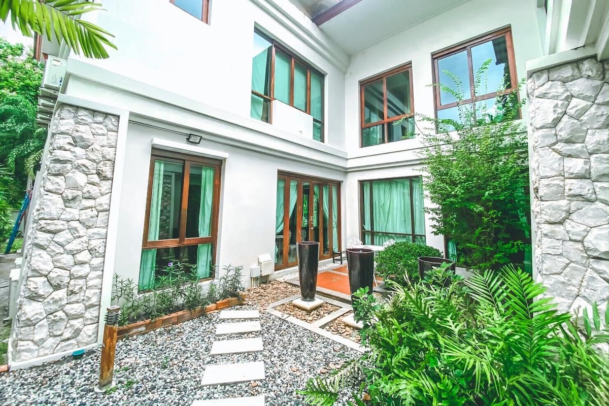 Uma casa moderna de dois andares, com grandes janelas, paredes de pedra e um jardim com pedras no caminho.
