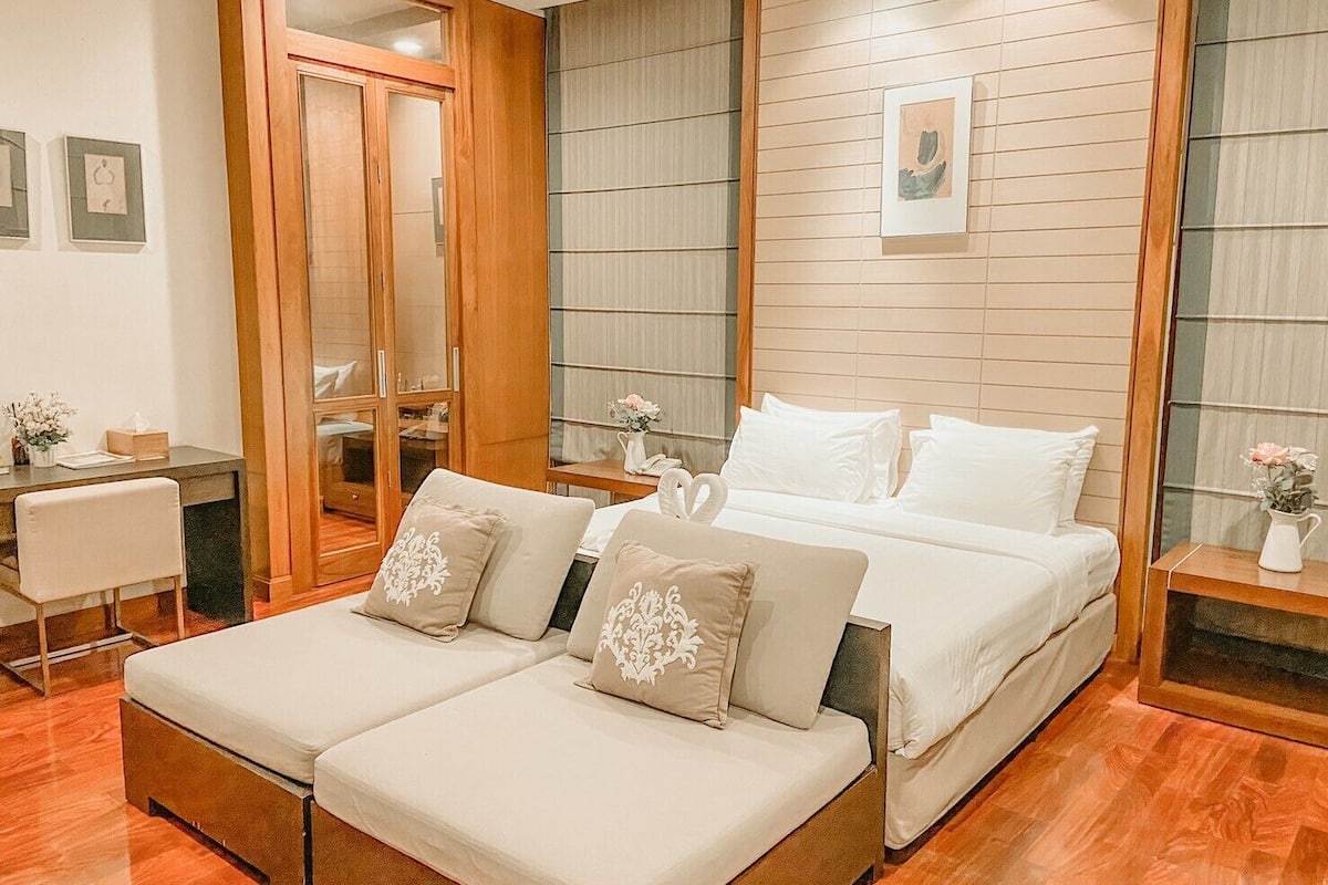 Quarto moderno com piso de madeira, cama com roupa de cama branca, escrivaninha com cadeira e um espelho grande.