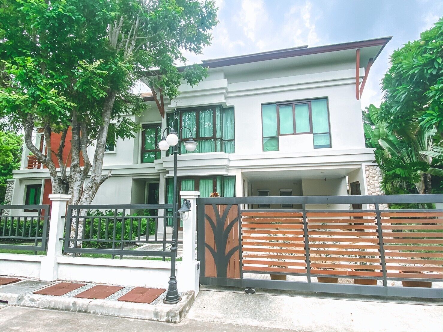 A modern two-story house with a gated entrance, a balcony, and a well-maintained garden.