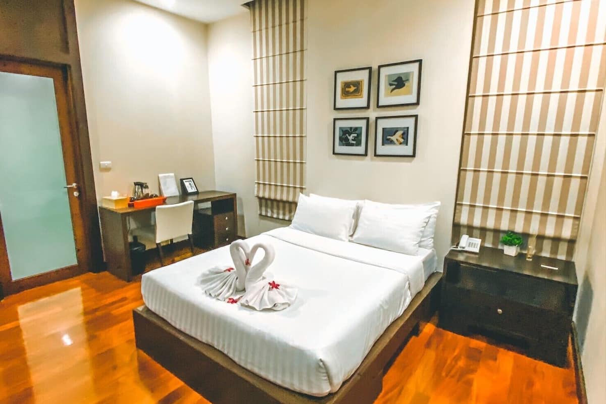 Quarto de hotel com cama, escrivaninha, cadeira, mesa de cabeceira e parede com quadros.